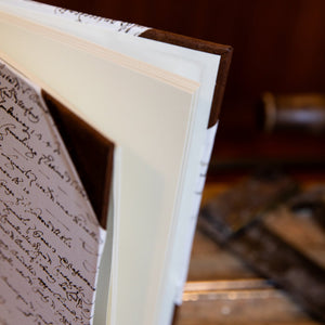 Open SB Libris half leather journal revealing thick, blank cream pages and vintage script endpapers.