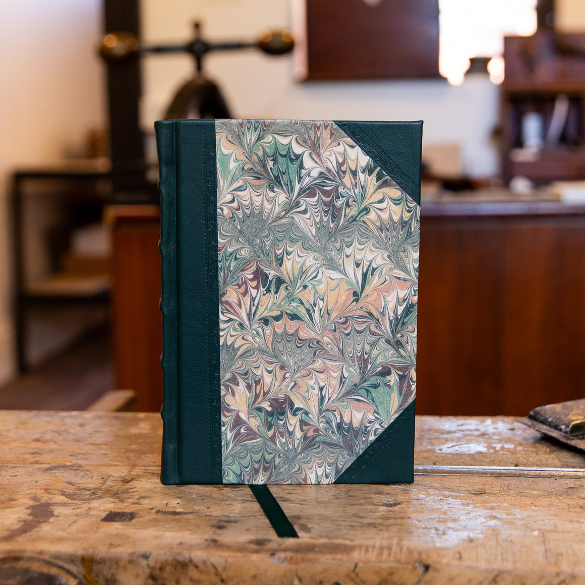 Close-up of the small Autumn Bouquet half leather journal, bound in dark green goatskin with marbled paper in autumn-inspired hues.