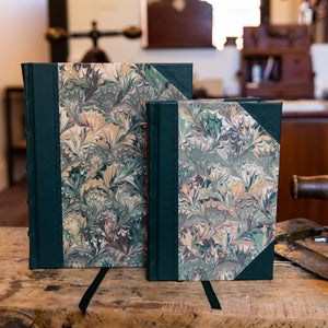 A pair of handcrafted SB Libris half leather journals in the Autumn Bouquet design, featuring deep green leather and swirling marbled paper in earthy tones.