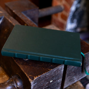 Green SB Libris full leather journal lying flat on a traditional bookbinder’s finishing press, showing spine ridges and smooth grain leather.