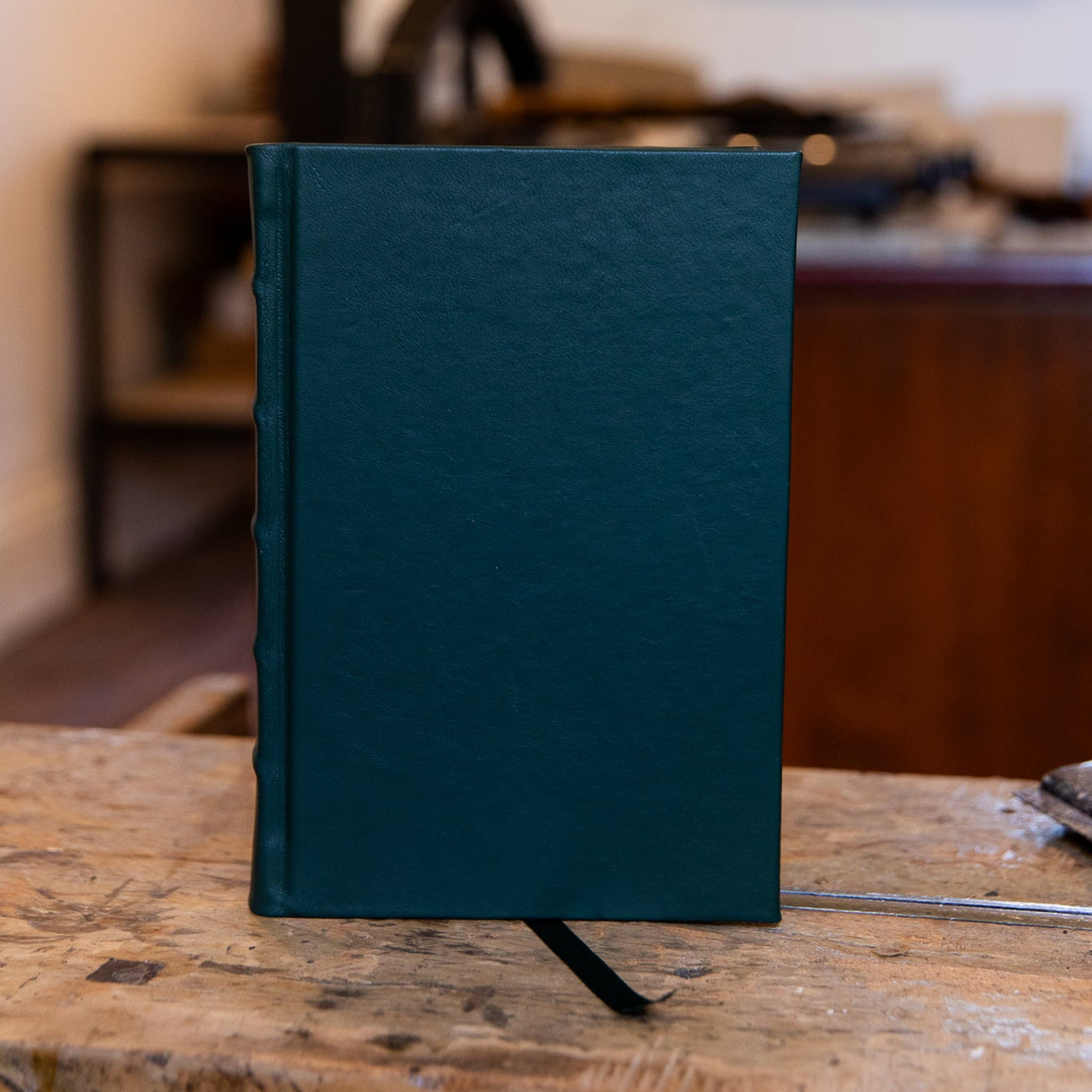 Smaller SB Libris green leather journal shown upright on the workbench, featuring subtle natural texture and handcrafted detail.