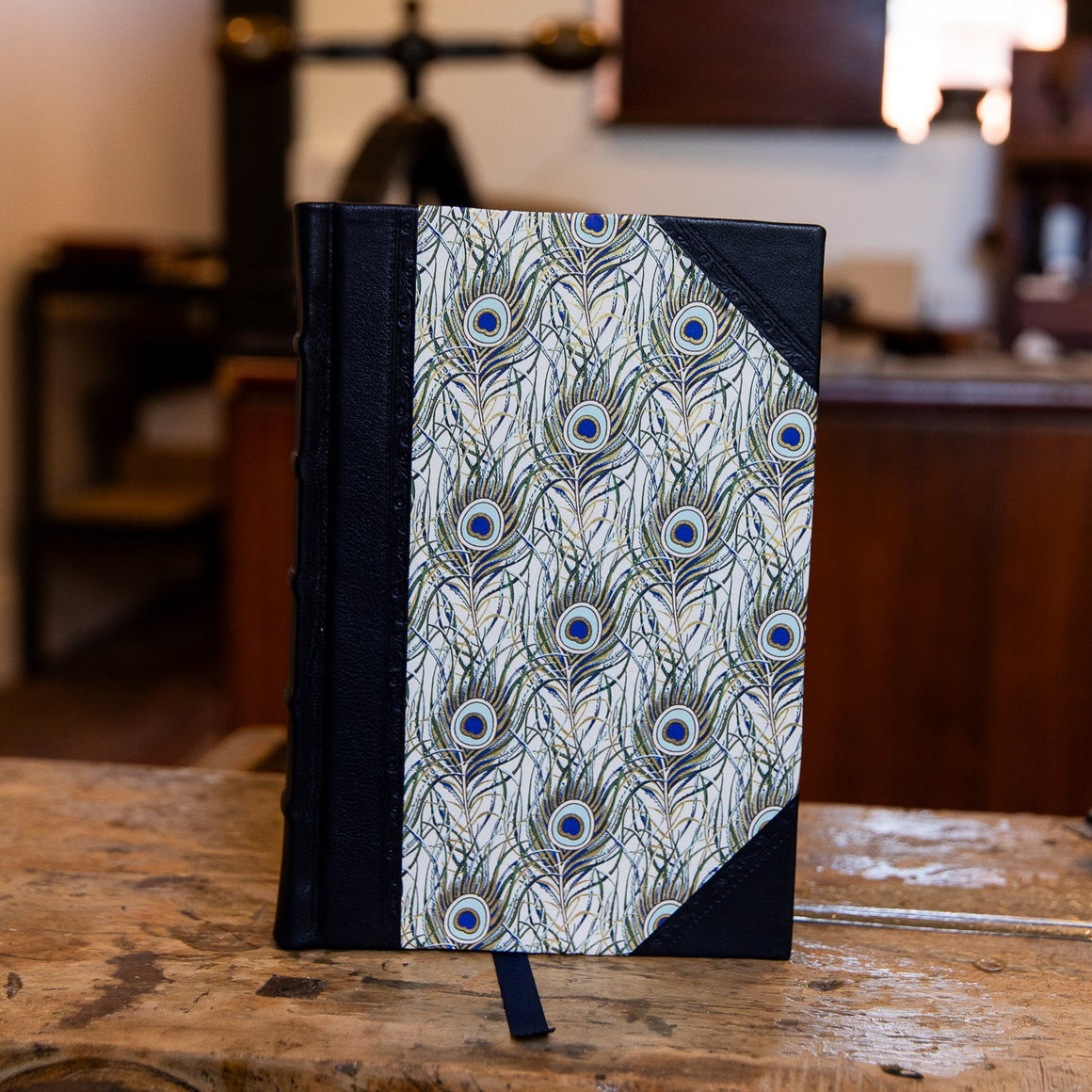 Handbound small half leather journal by SB Libris with navy leather and intricate peacock feather patterned paper.