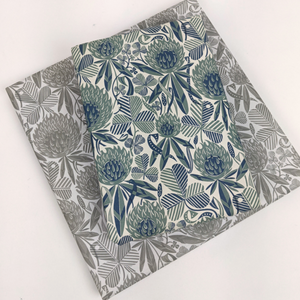 A large gift square gift wrapped in the grey clover design.  A smaller gift wrapped in The teal coloured clover design sits on top
