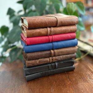 The spines of a small pile of leather wrap journals in a variety of colours