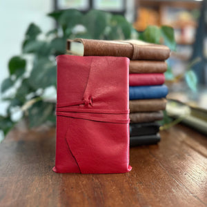 A Scarlett red leather wrap journal placed in front of a pile of leather wrap journals